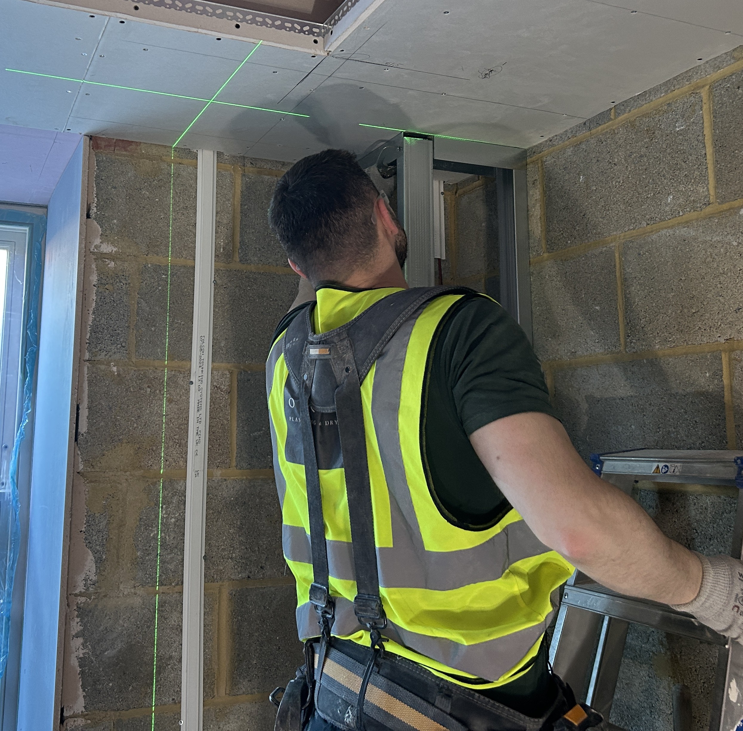 Construction worker inspecting plasterboard ceiling installation and metal framing on site